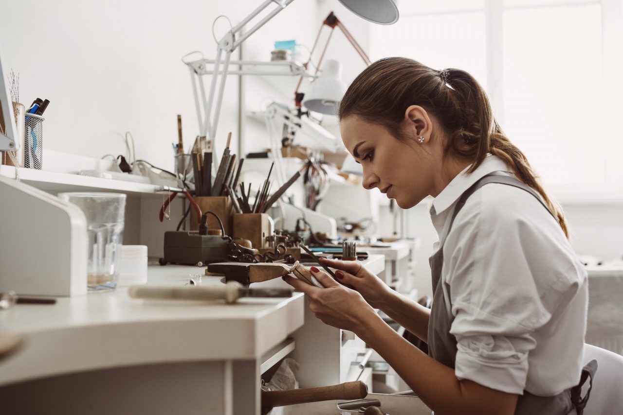focused on a process portrait of young female jeweler focused on creating a silver ring at her